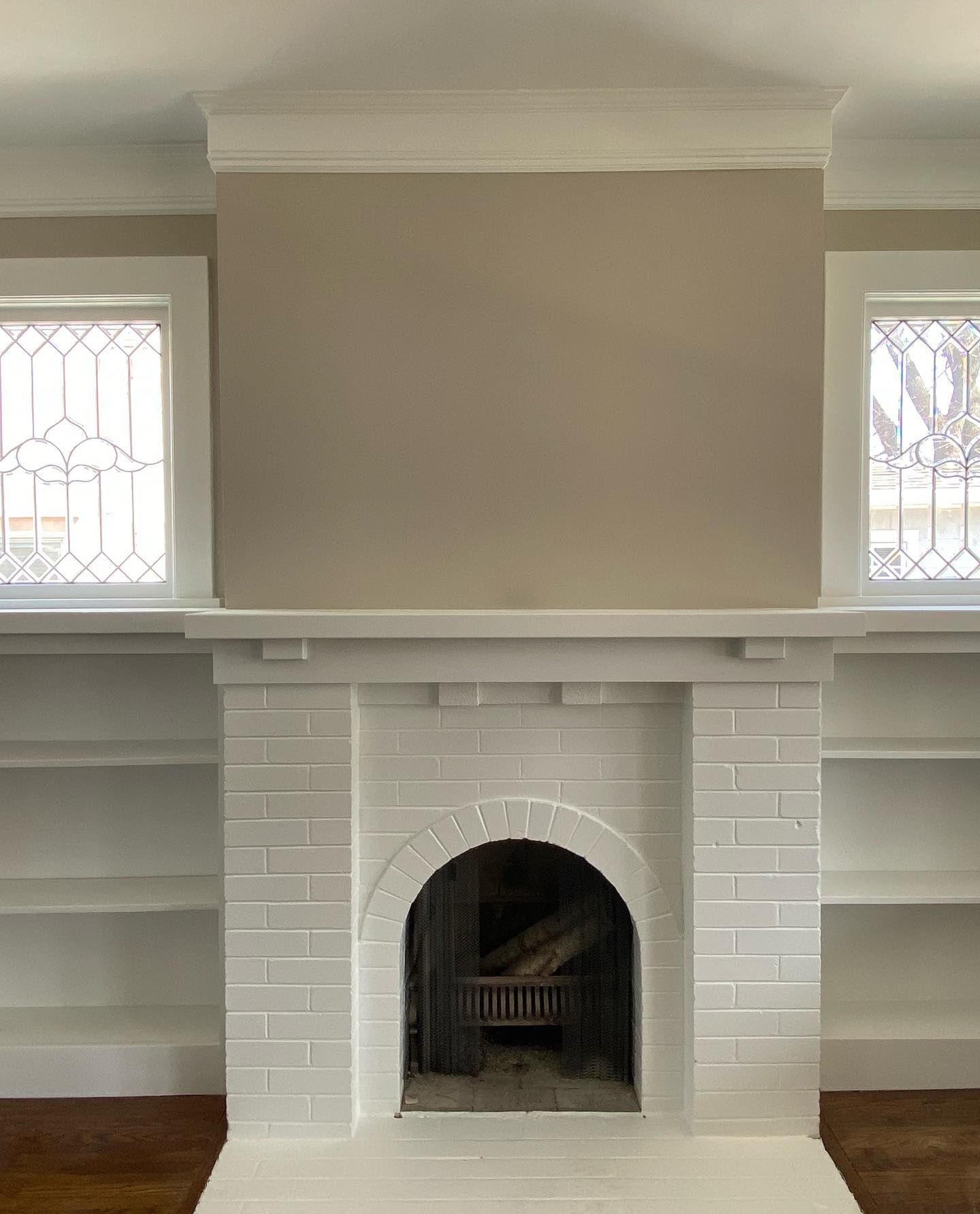 White brick fireplace with arched opening and built-in shelves. Beige wall above, flanked by windows.