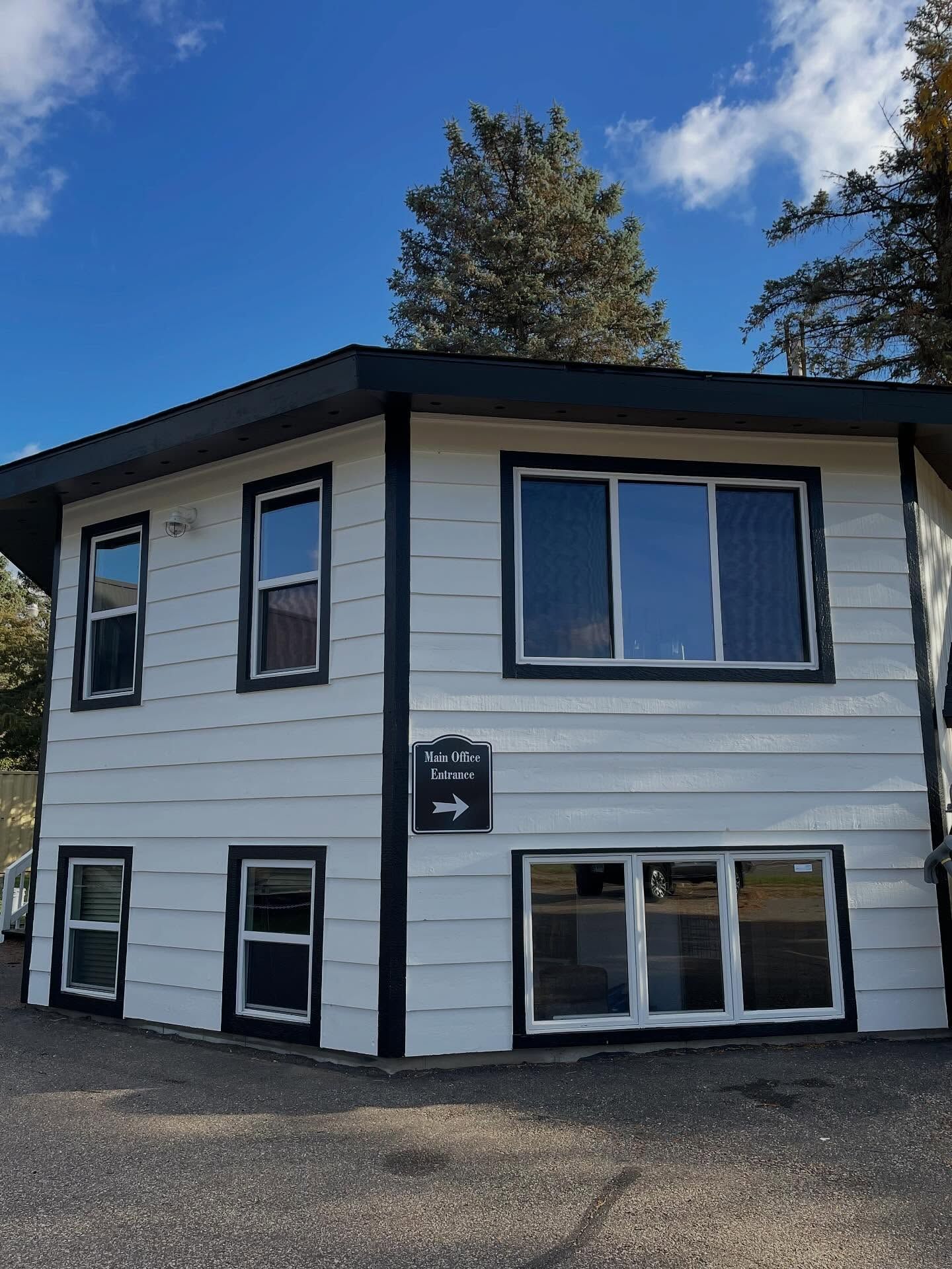 Two-story white building with black trim. Windows are visible. A blue sky is above.