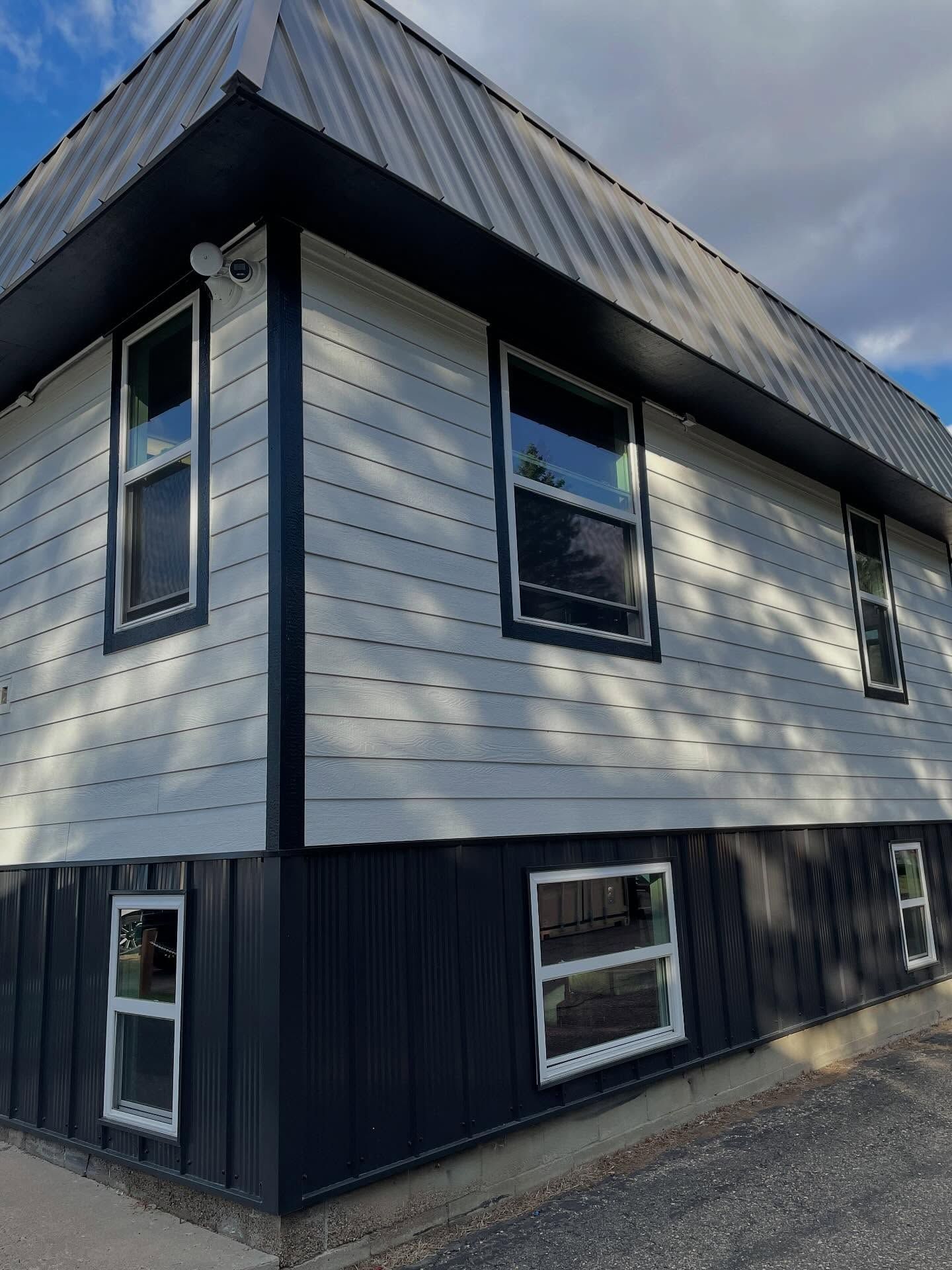 Two-story building with gray siding, black trim and metal roof. Several rectangular windows.