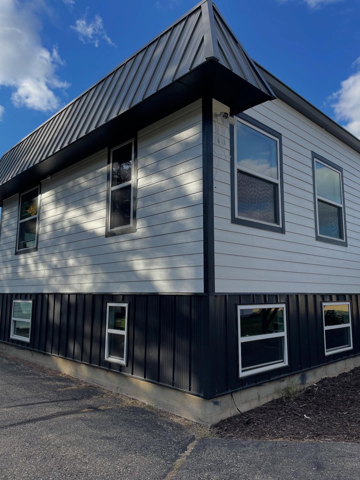 Two-story building with white siding, dark trim, and metal roof. Windows are framed in white.