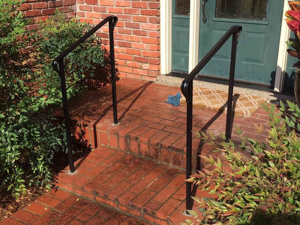 A black railing is sitting on a brick walkway next to a green door