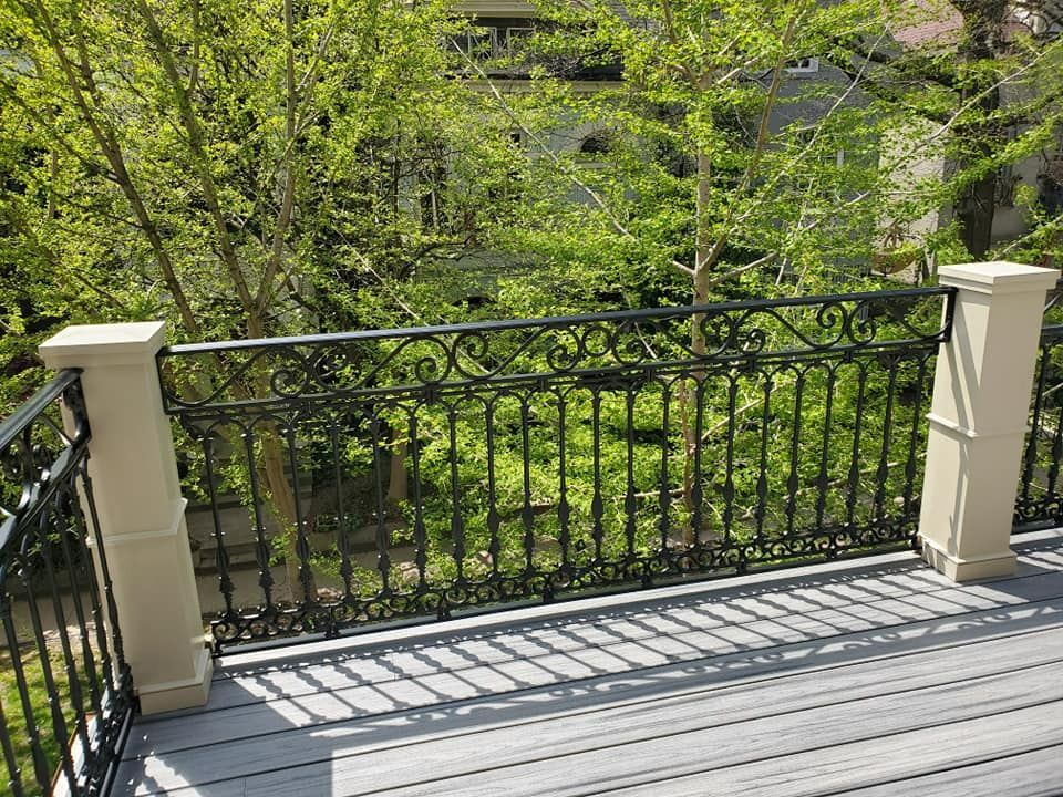 A balcony with a wrought iron railing and trees in the background