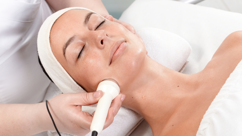 Person receiving a facial treatment with a handheld device at a spa.