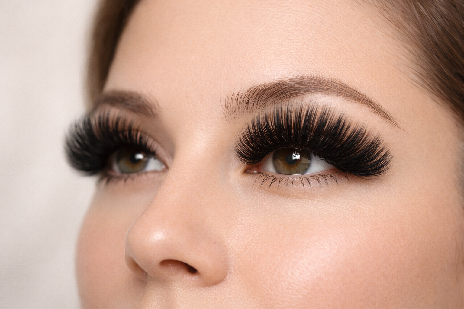Woman's face with dramatic, thick black eyelash extensions. Brown eyebrows, pale skin, soft focus.