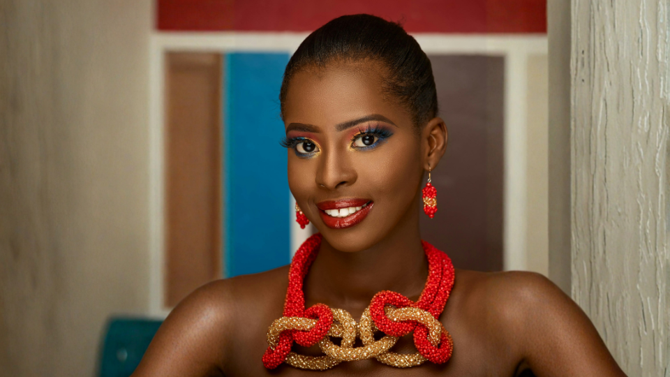 Woman with dark skin wearing red and gold jewelry, smiling at the camera.