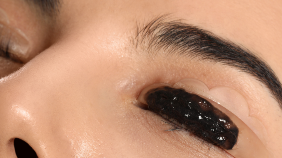 Person's eyelid with black substance inside, held by clear tape.
