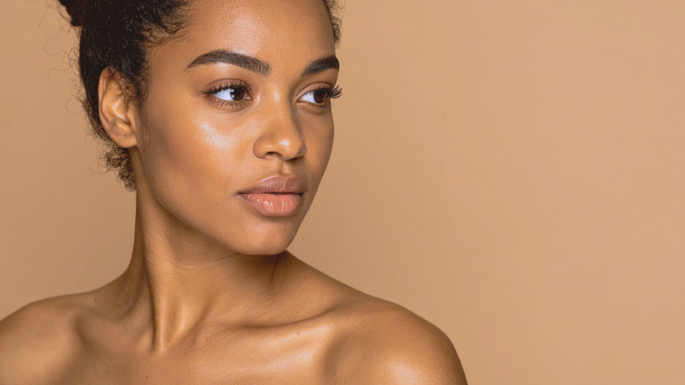 Woman with smooth, glowing skin looking to the side. Light beige background.