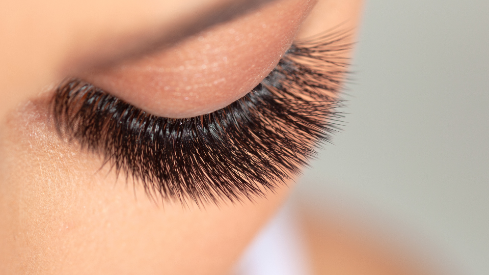 Close-up of a closed eye with long, dark eyelashes. Light skin is visible.