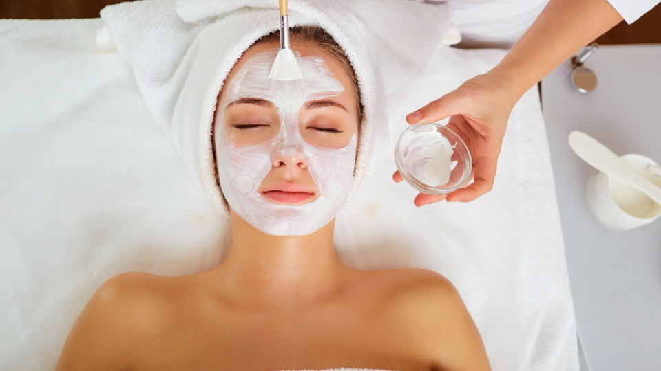 Woman receiving facial treatment, white mask applied by a spa professional, spa setting.