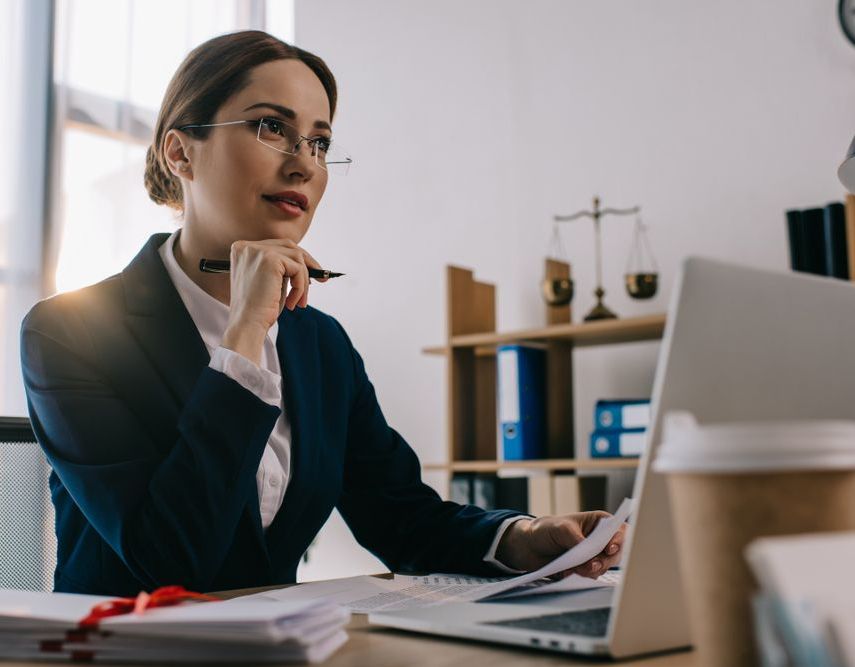 A Woman Is Sitting At A Desk In Front Of A Laptop Computer — Charlestown Law Firm In Maitland, NSW