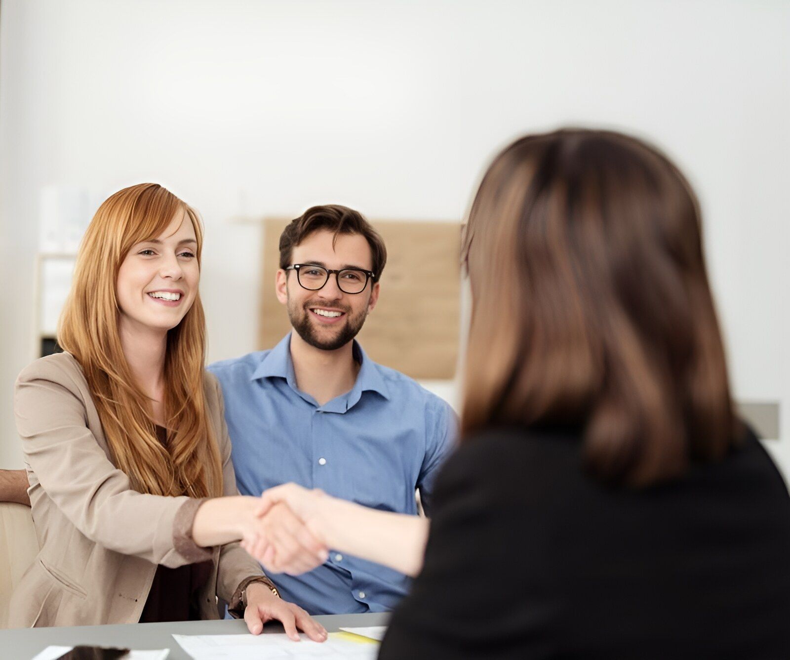 A Man And Woman Are Shaking Hands With A Woman While Sitting At A Table — Charlestown Law Firm In Charlestown, NSW
