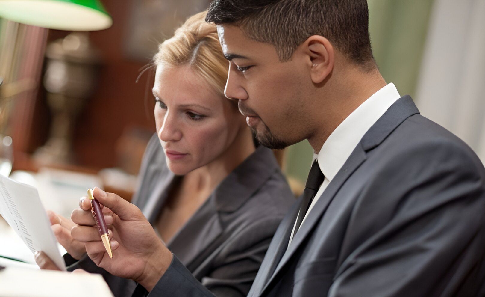A Man And A Woman Are Sitting At A Table Looking At A Piece Of Paper — Charlestown Law Firm In Sydney, NSW