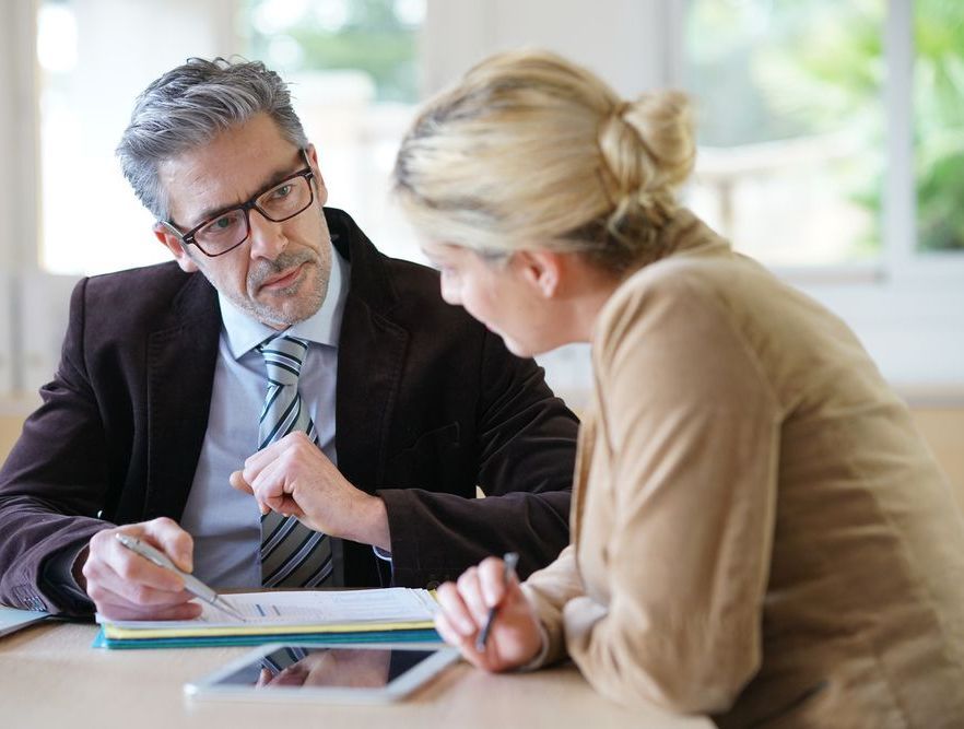 A Man And A Woman Are Sitting At A Table Looking At A Tablet — Charlestown Law Firm In Newcastle, NSW