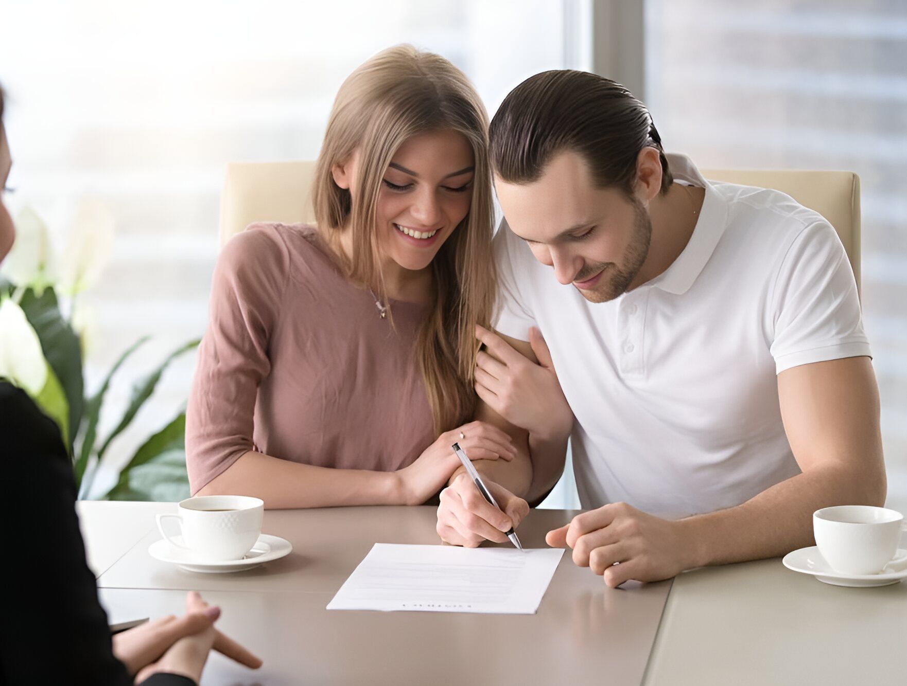 A Man And A Woman Are Sitting At A Table Signing A Document — Charlestown Law Firm In Charlestown, NSW