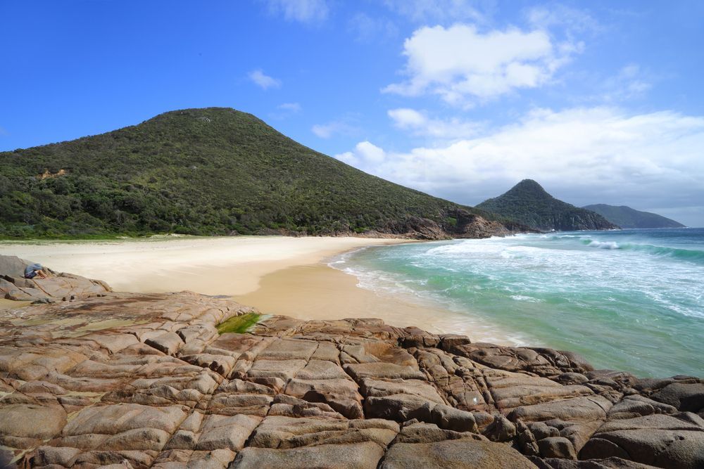 A Beach With A Mountain In The Background And Rocks In The Foreground — Charlestown Law Firm In Port Stephens, NSW