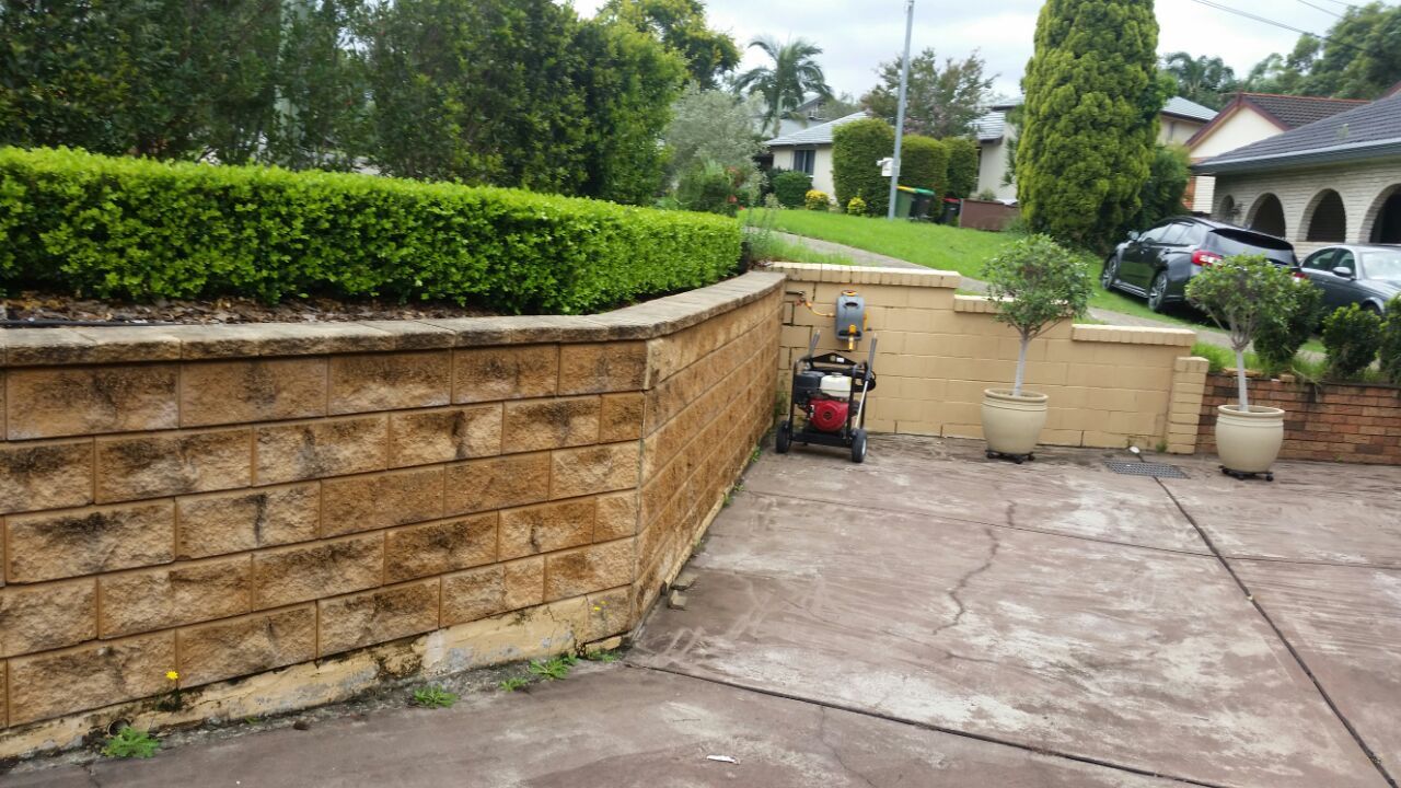A brick wall with a lawn mower parked in front of it.