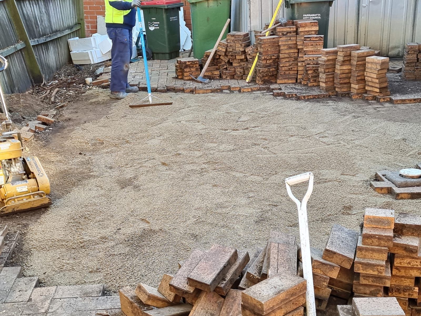 A man is sweeping the ground next to a pile of bricks.