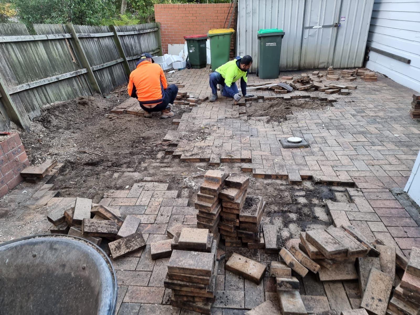 Two men are working on a brick patio.