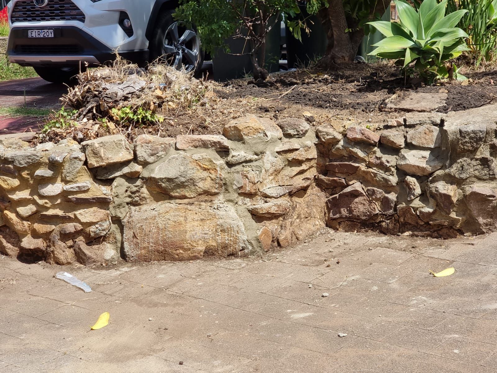 A white car is parked in front of a stone wall.