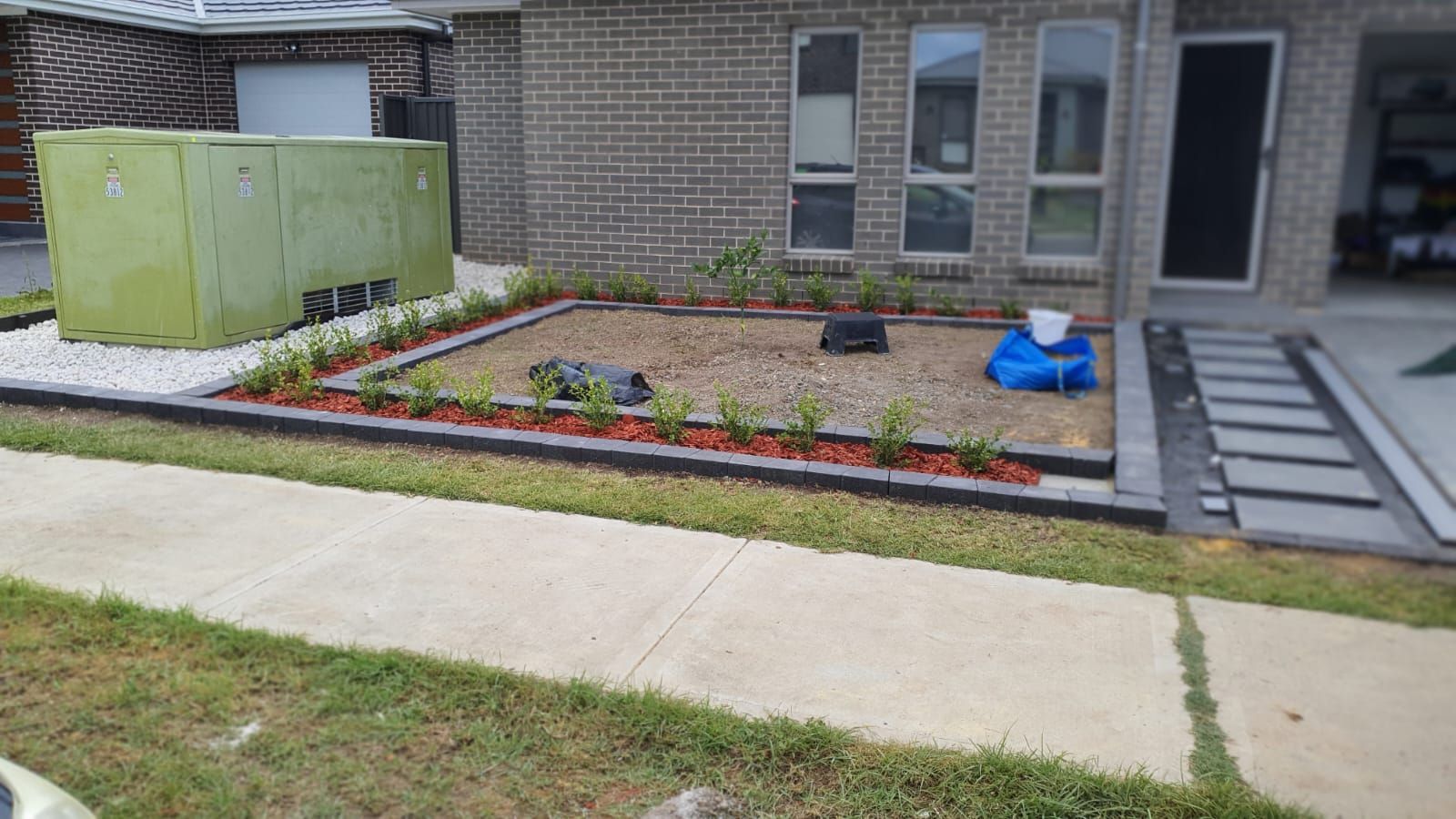 A brick house with a garden in front of it and a sidewalk.