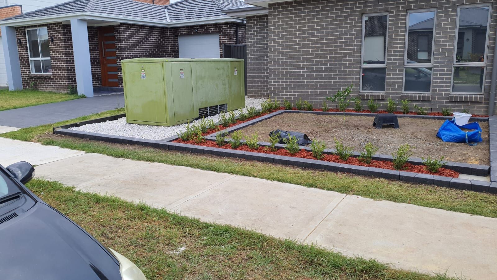 A black car is parked in front of a brick house.