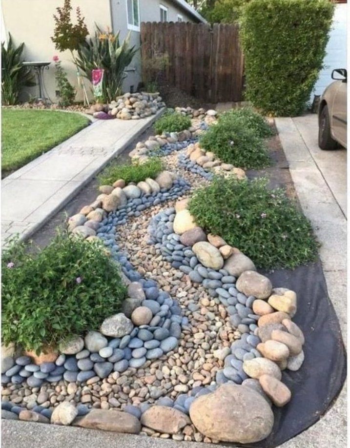 A car is parked in a driveway next to a rock garden.