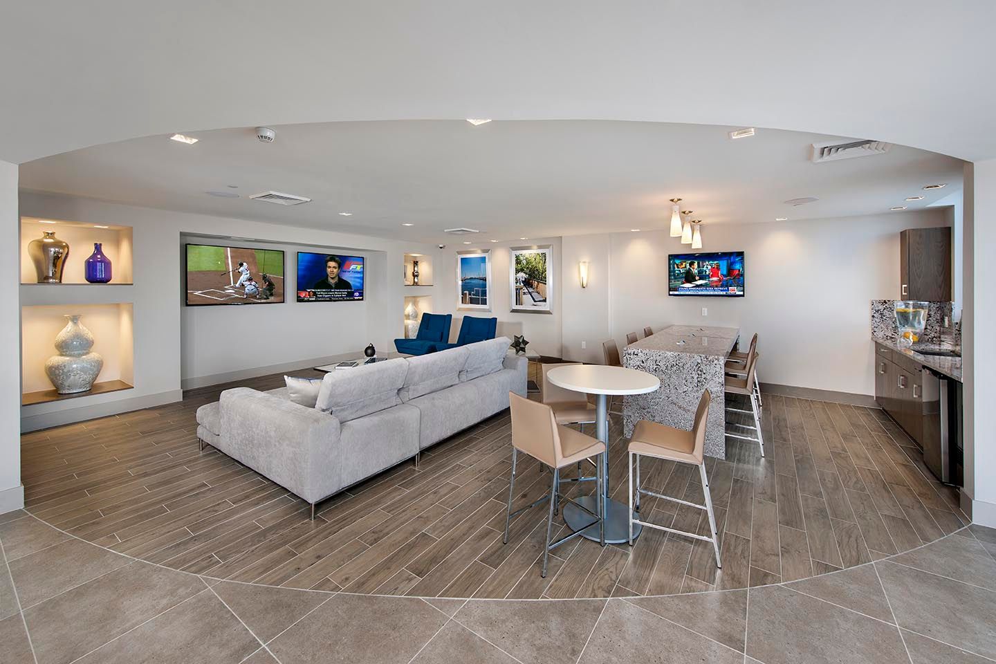 Modern community lounge with couches, TVs, dining table, and bar area.