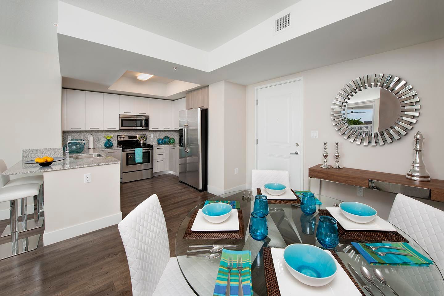 Open-concept kitchen and dining area with white cabinets, stainless steel appliances, and a glass-top table set for dining.