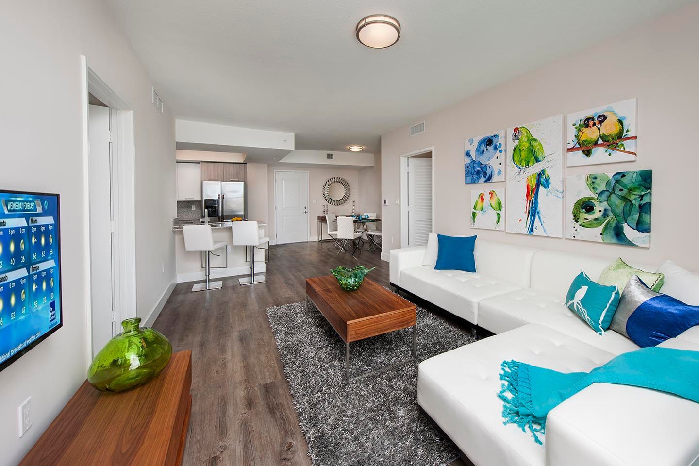 Modern apartment living room with white sectional sofa, art, and open kitchen.