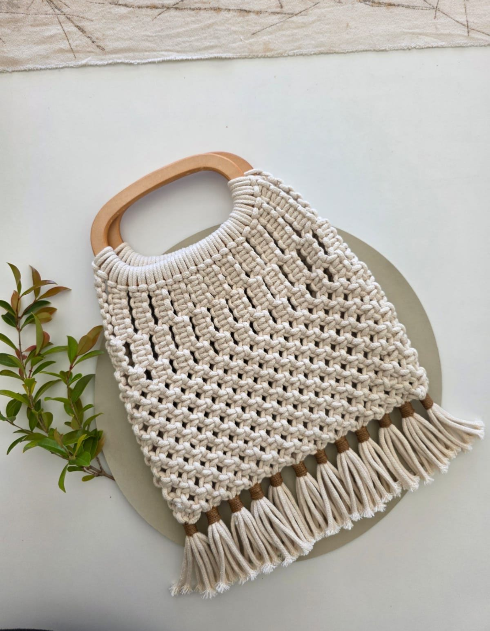 Bolso tote de macramé con asas de madera sobre superficie neutra.
