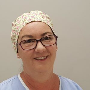 A woman wearing glasses and a surgical cap is smiling for the camera.