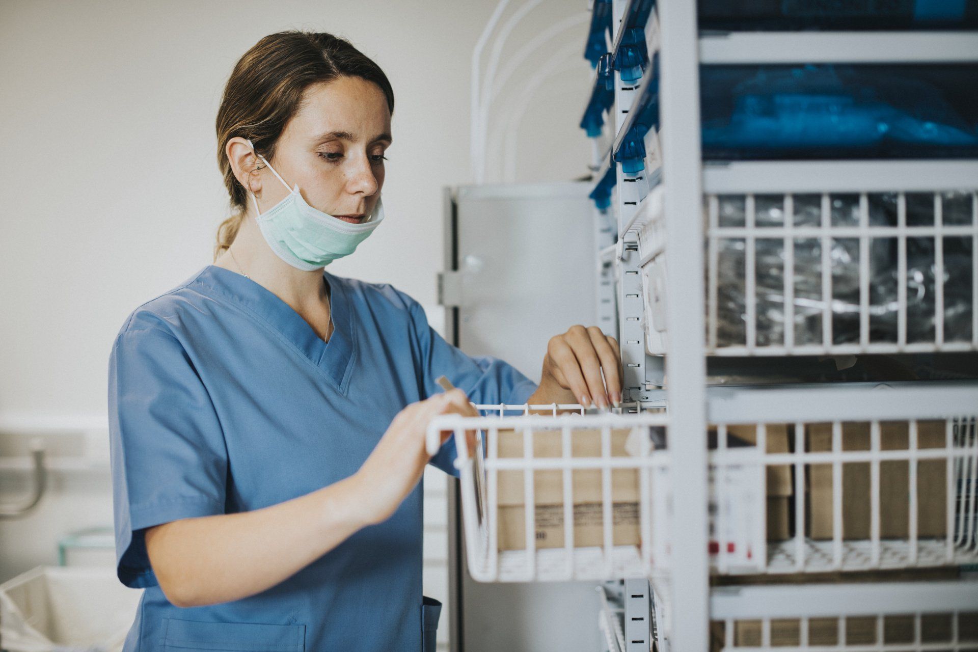 A nurse wearing a mask is looking at a basket in a hospital.