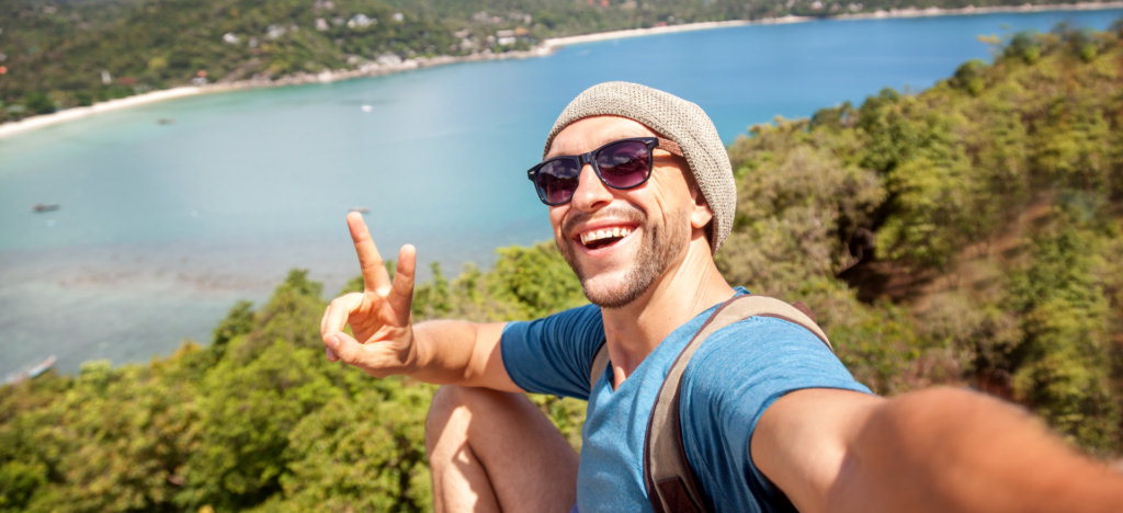 A man is taking a selfie on top of a hill overlooking the ocean.