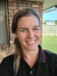 A woman in a black shirt is smiling in front of a brick building.