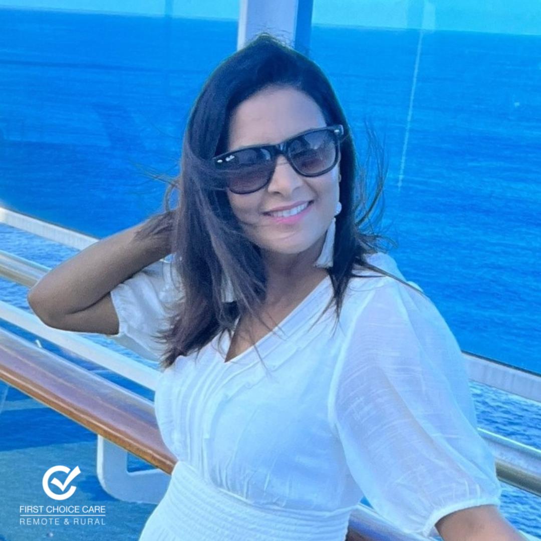 A woman wearing sunglasses and a white dress stands on a balcony overlooking the ocean