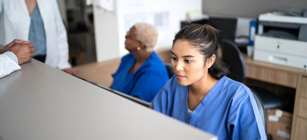 A nurse is sitting at a desk in a hospital talking to a doctor.