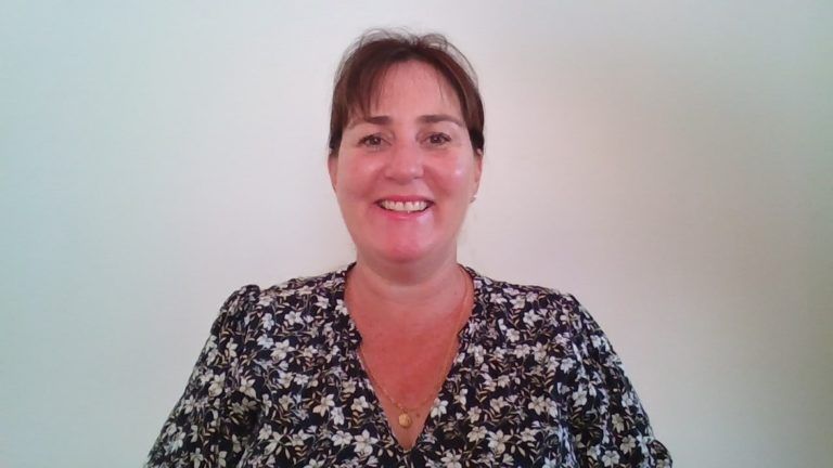 A woman in a floral shirt is smiling for the camera.