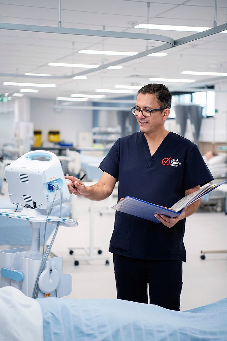 A man in a blue scrub is standing in a hospital room looking at a monitor.