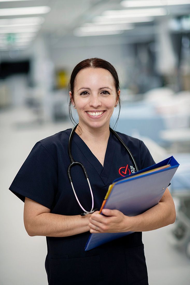 A nurse with a stethoscope around her neck is holding a clipboard in a hospital.