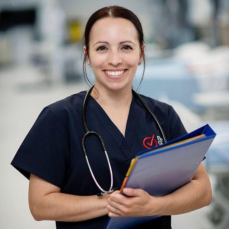 A nurse with a stethoscope around her neck is smiling and holding a clipboard