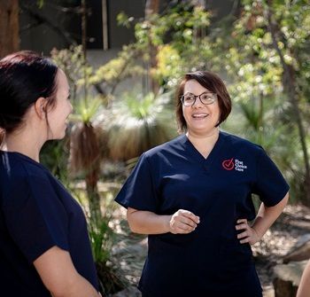 Two women in scrubs are standing next to each other and smiling