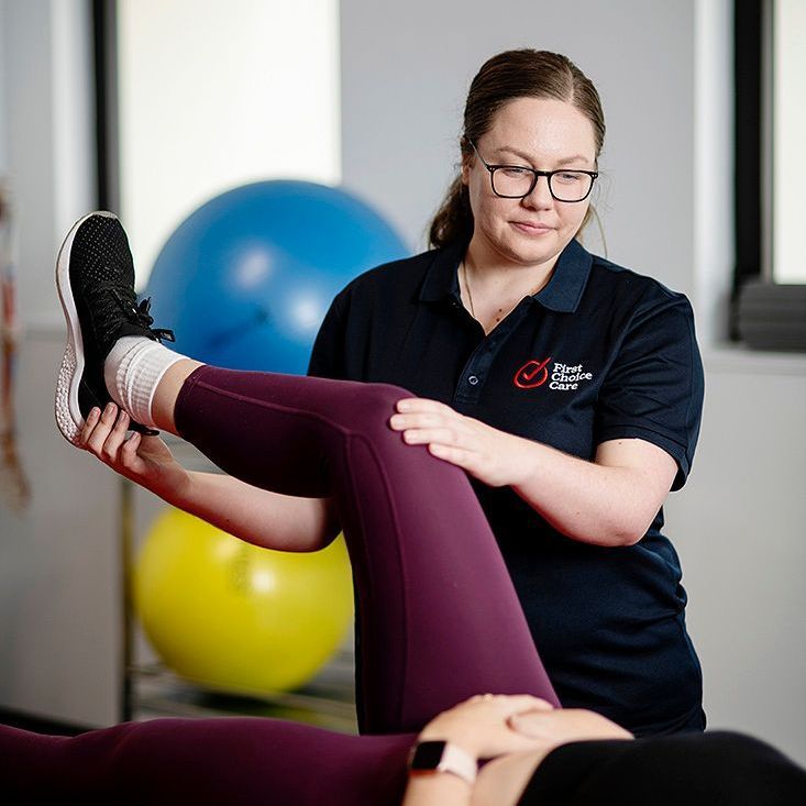 A woman is stretching another woman 's leg in a gym.