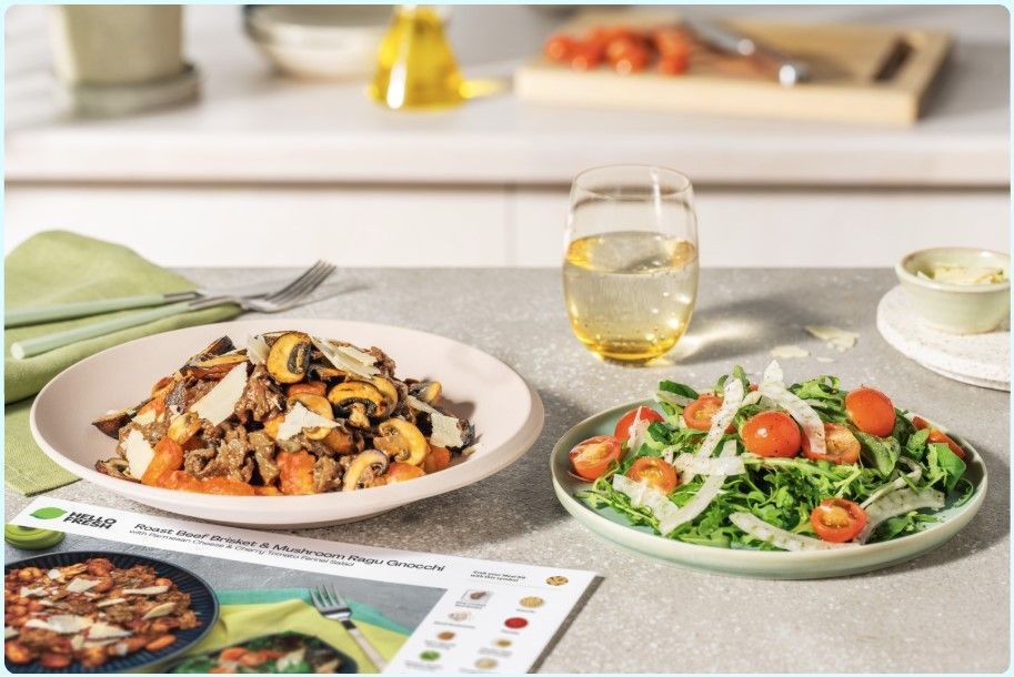Plate of pasta with mushrooms, salad with tomatoes, glass of water, kitchen setting.