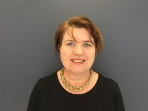 A woman wearing a black shirt and a gold necklace is smiling for the camera.