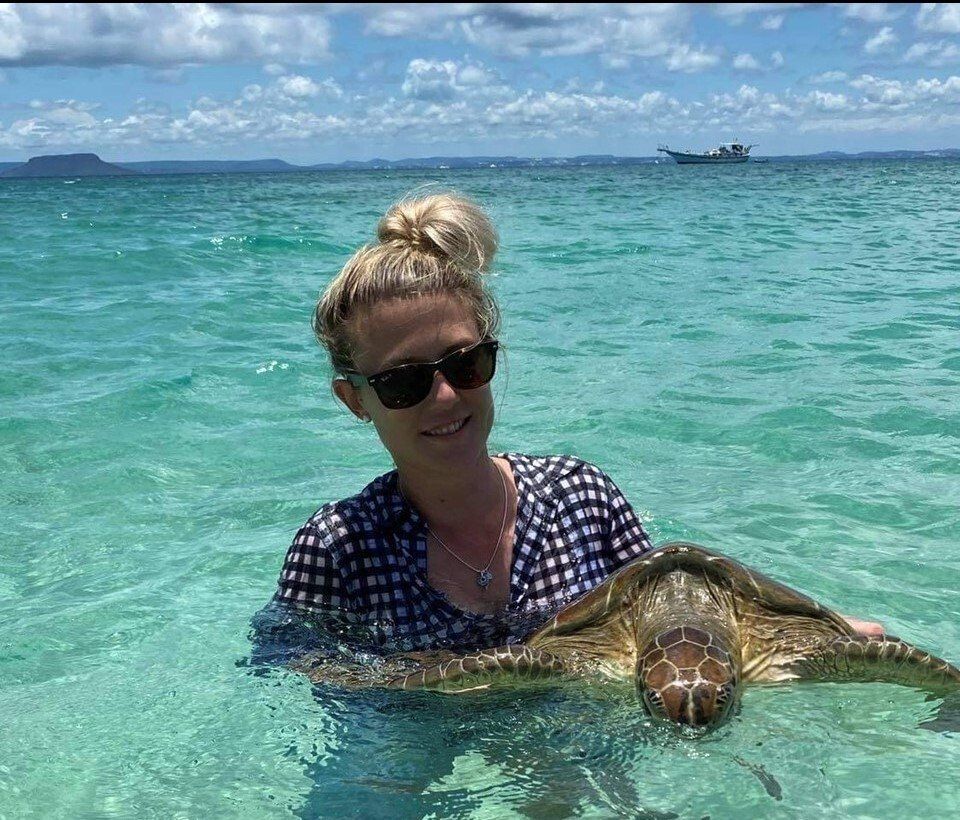 A woman is holding a sea turtle in the ocean.