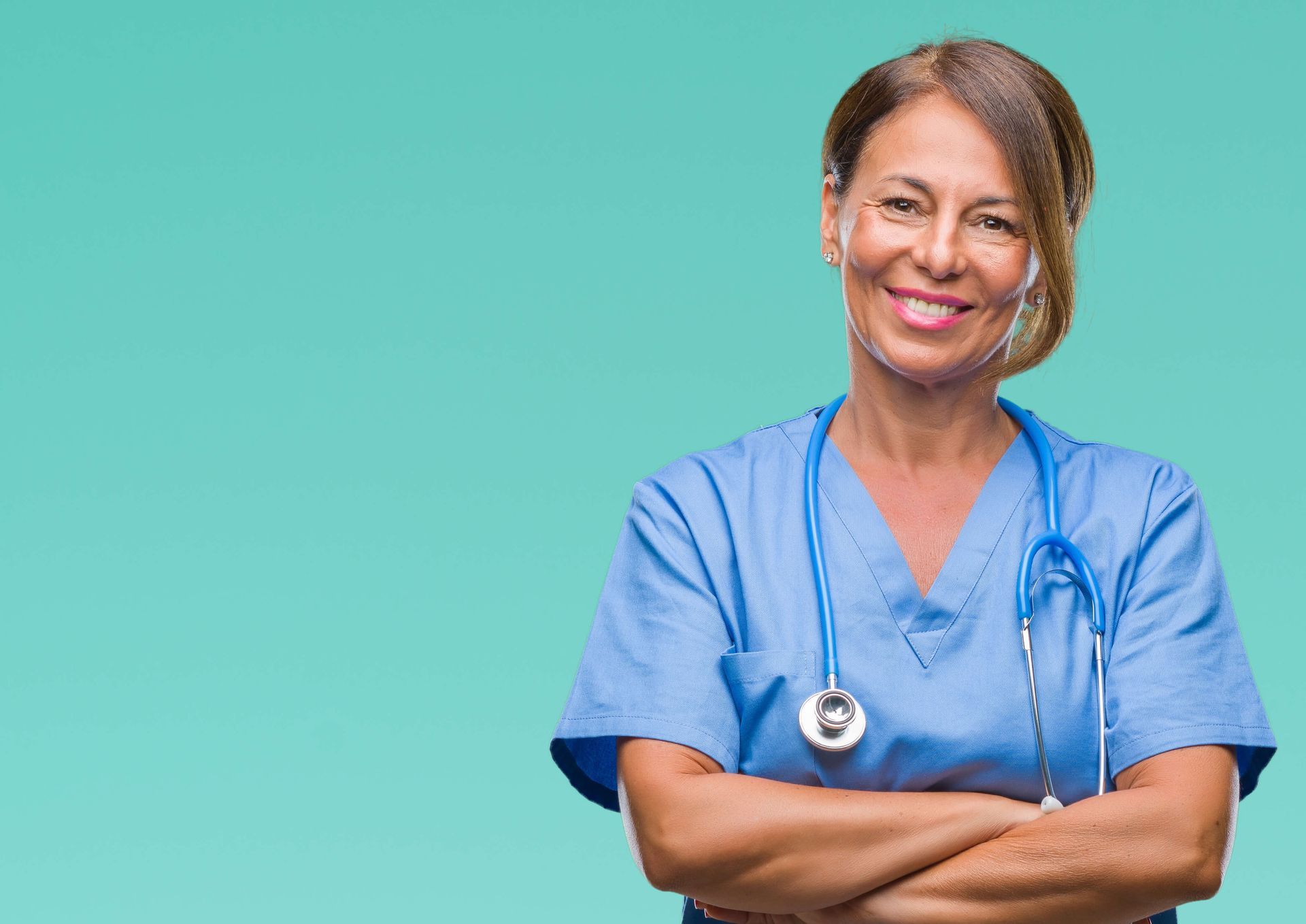 A nurse with a stethoscope around her neck is smiling with her arms crossed.