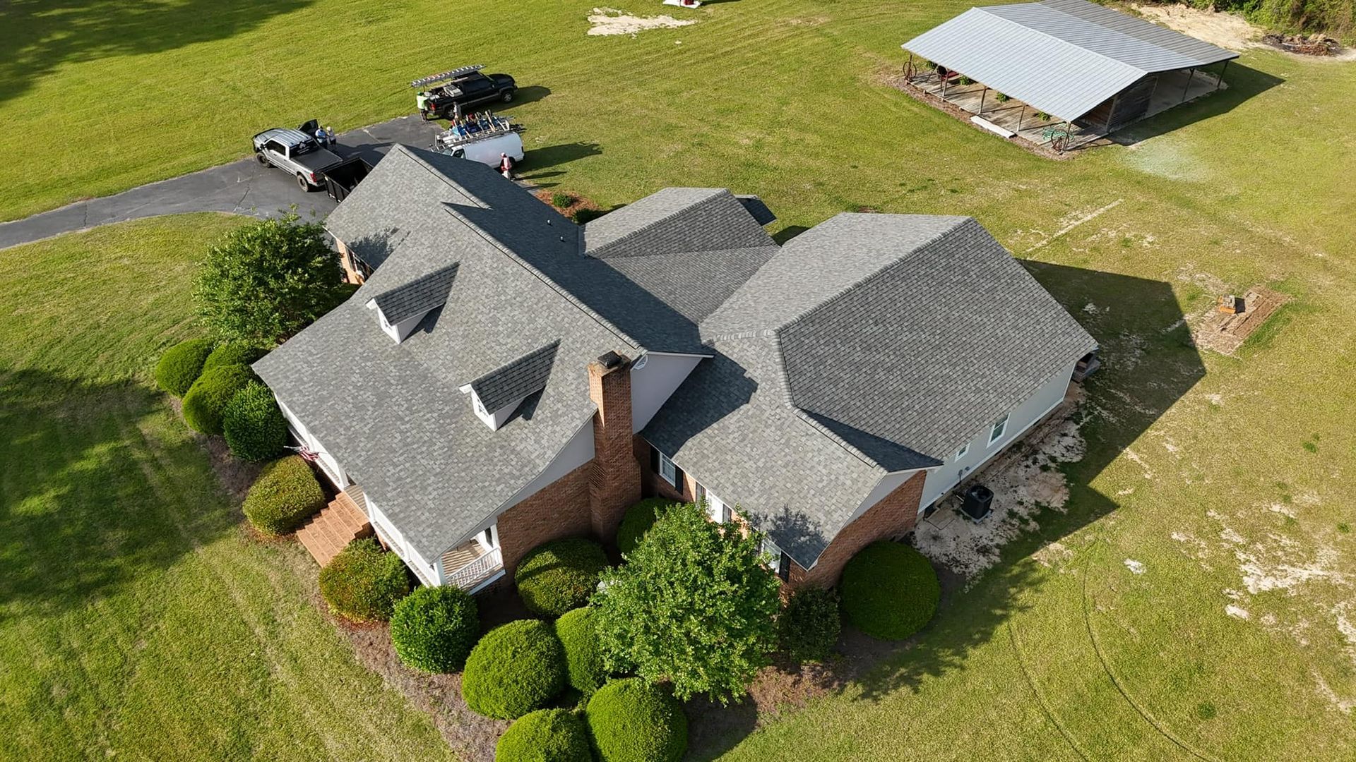 An aerial view of a large house with a carport in the background.