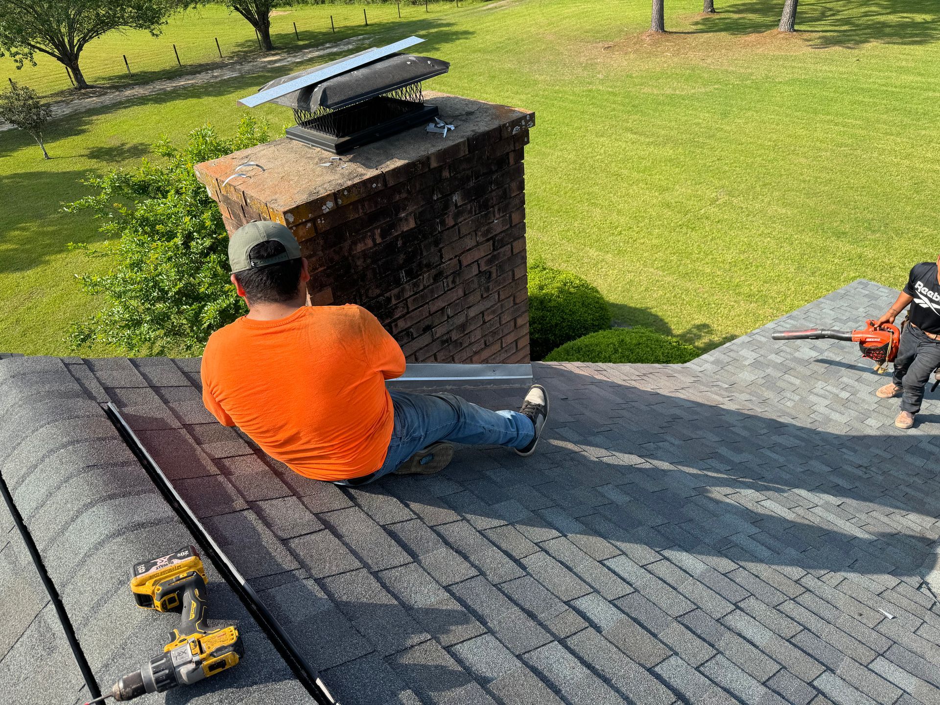A man is sitting on top of a roof next to a chimney.