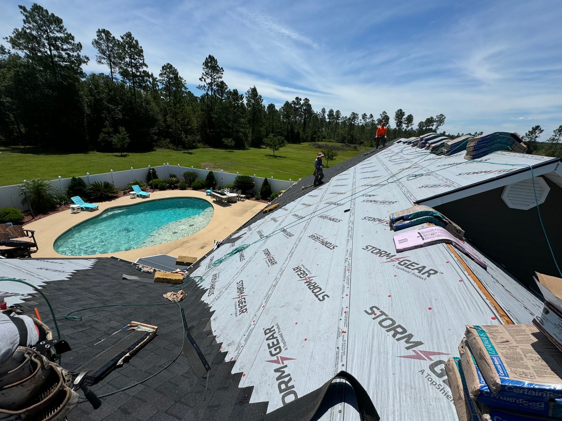 A man is working on the roof of a house with a pool in the background.