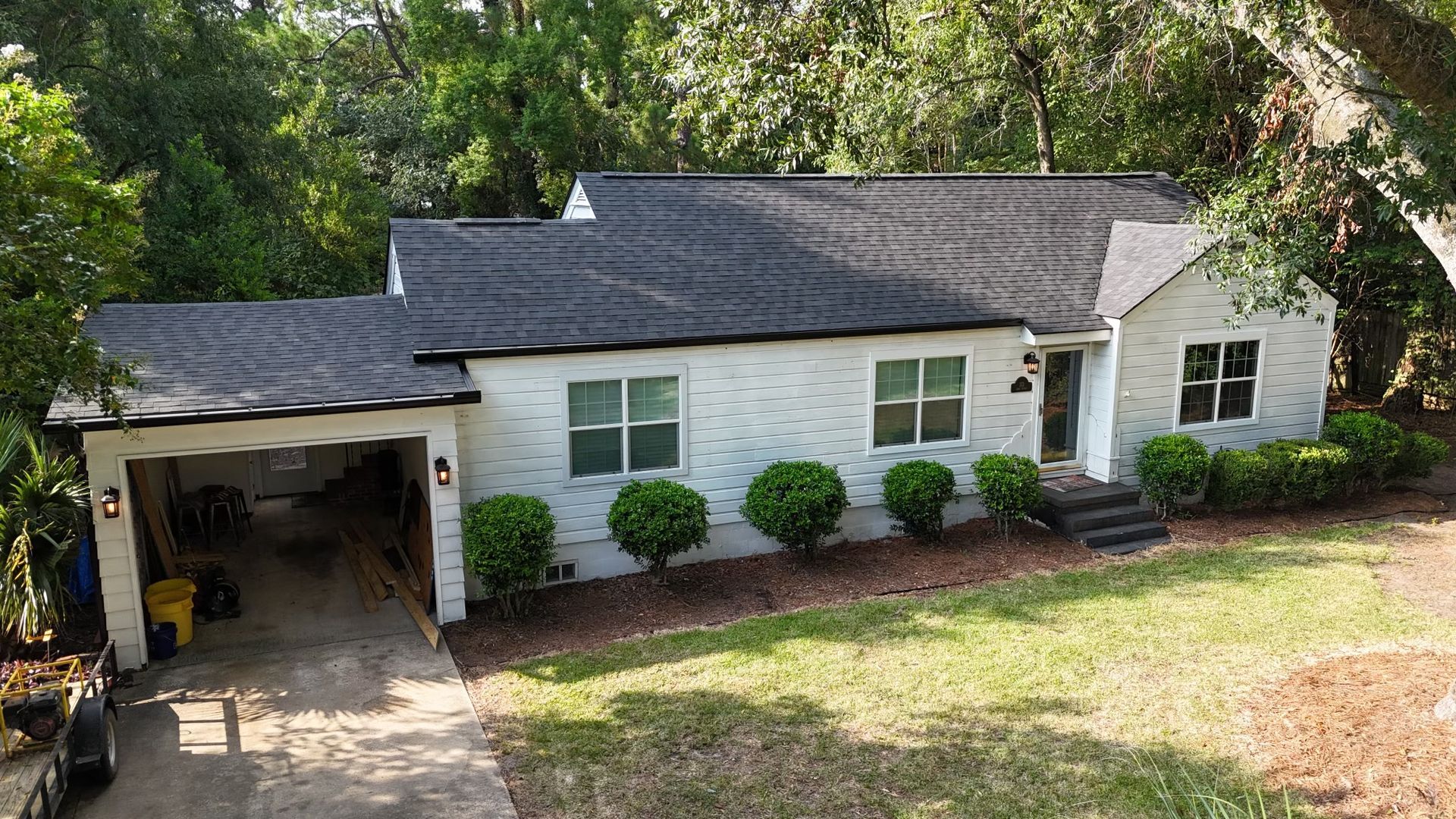 An aerial view of a white house with a black roof and a garage.